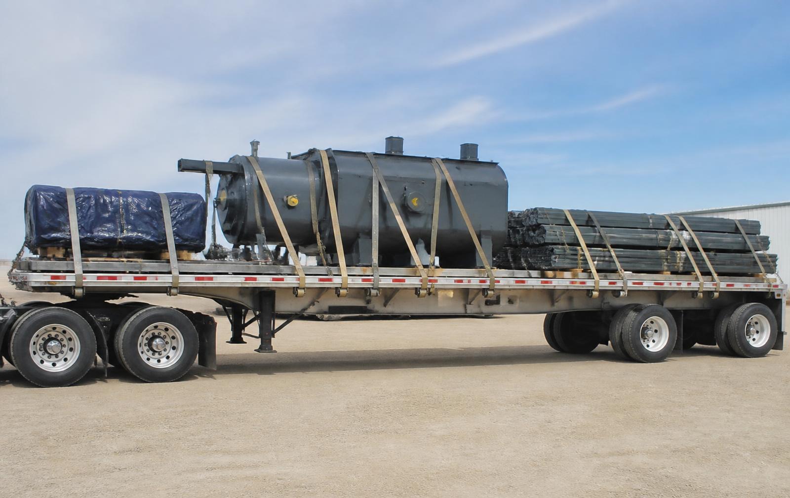 Plataforma transportando carga suelta y maquinaria asegurada con bandas.